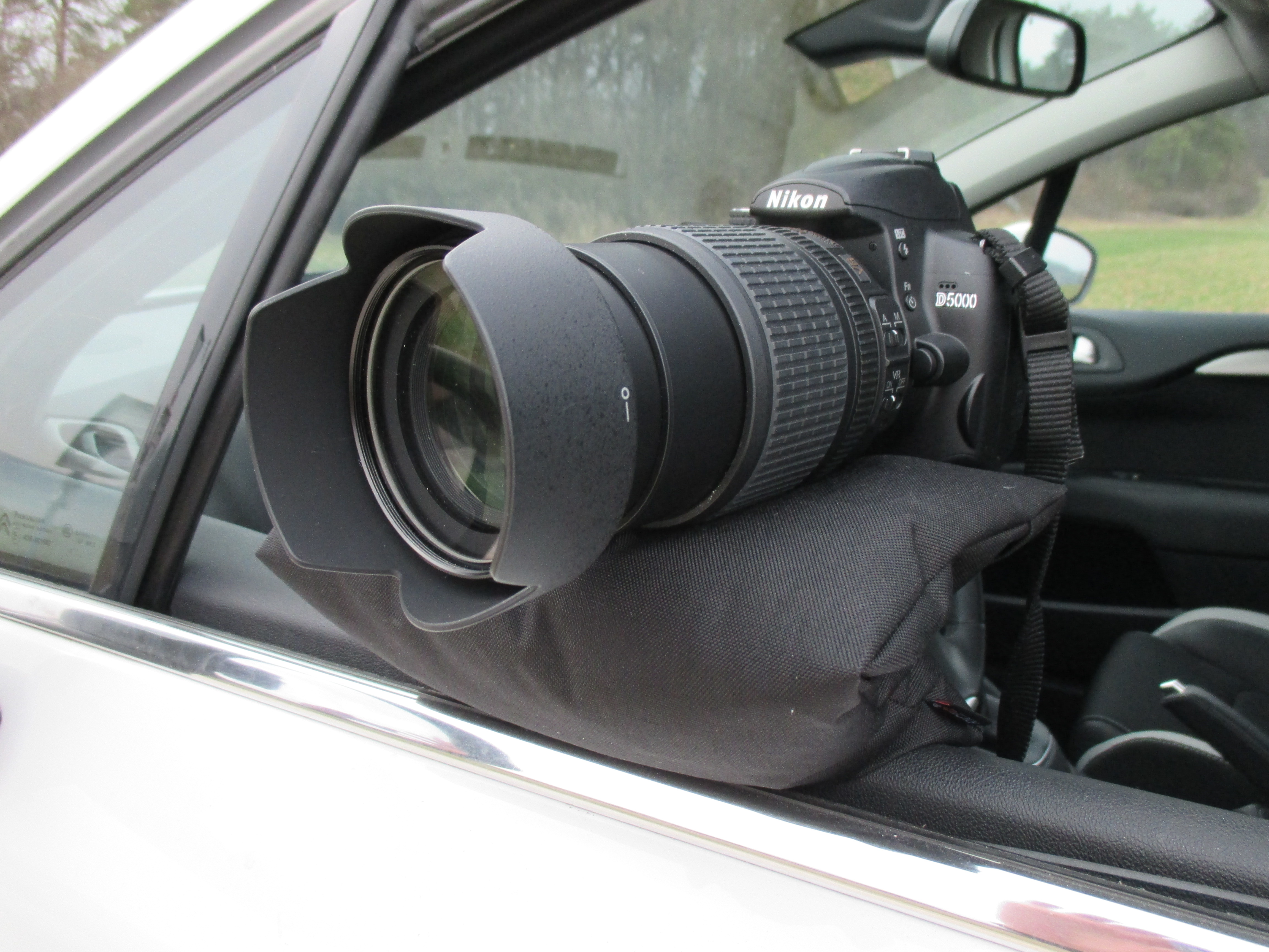 RiceQ Bohnensack Edition mit Spiegelreflexkamera und Teleobjektiv am offenen Autofenster