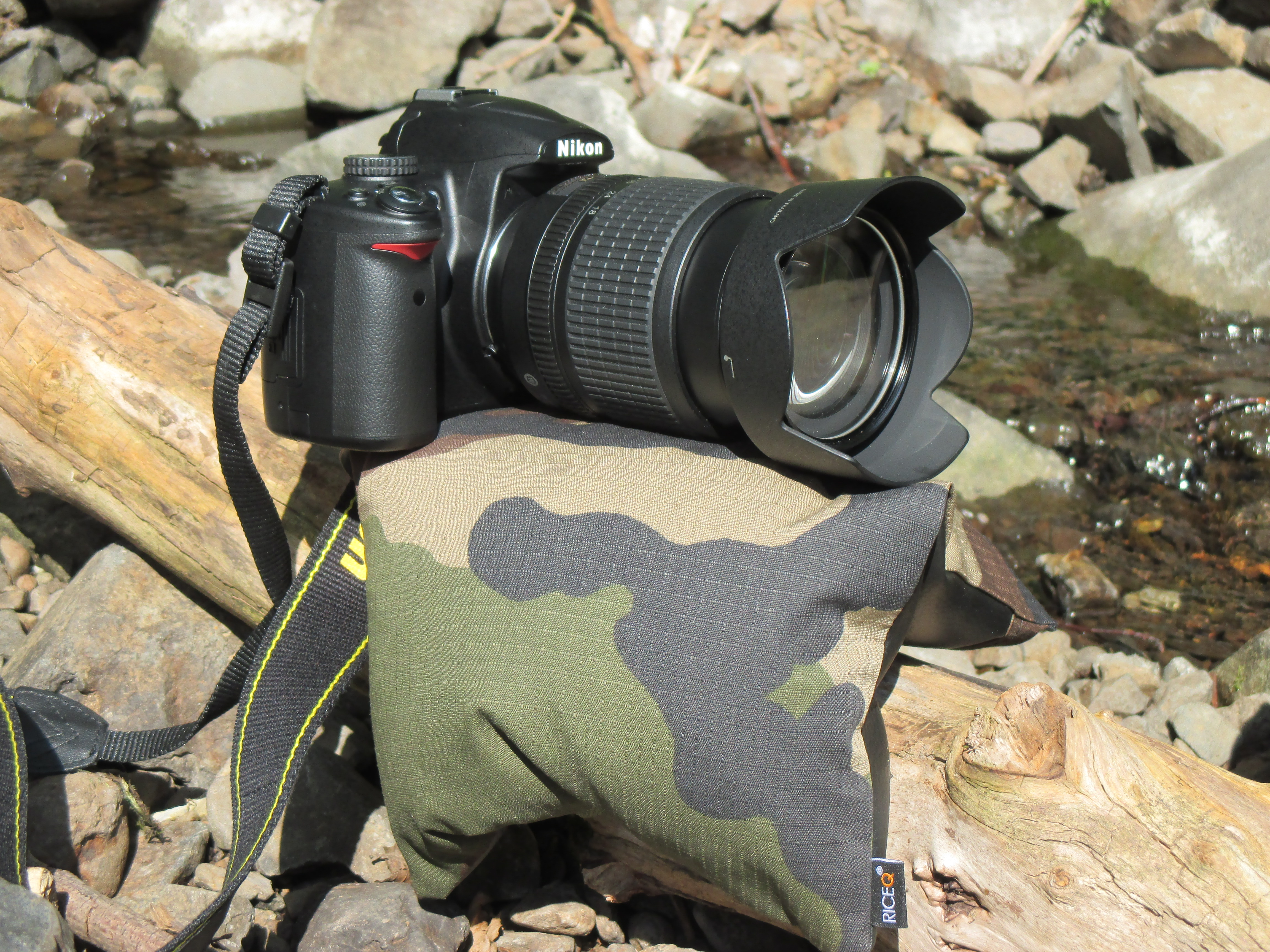 Kamera mit Teleobjektiv auf dem RiceQ Bohnensack Outdoor Oliv auf Felsen am Wasser
